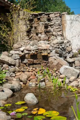 a stone wall next to a pond with lilies at Résidence U Pirellu in Porto-Vecchio