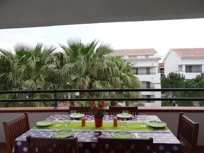 a table on a balcony with a view of palm trees at Vue sur mer et montagnes in Moriani Plage