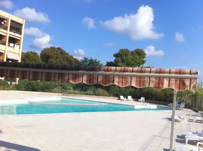 a swimming pool with awning and chairs and a building at Studio les pieds dans l'eau in Santa-Lucia-di-Moriani