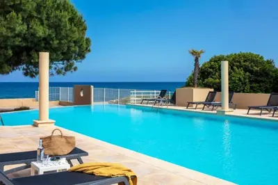 a swimming pool with chairs and the ocean in the background at Résidence Marina Bianca in Santa-Lucia-di-Moriani