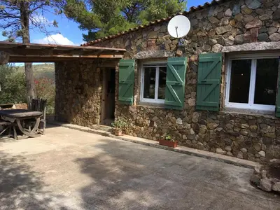 a stone house with green shuttered windows and a table at Maison de Campagne in Sarragia