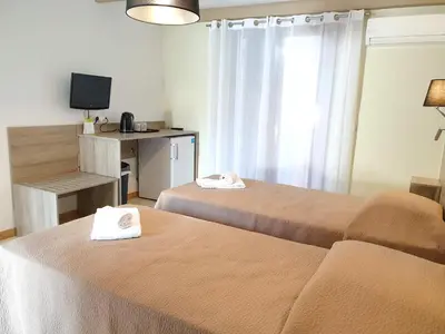 a room with two beds and a desk with a television at Hotel Olmuccio in Sainte-Lucie de Porto-Vecchio