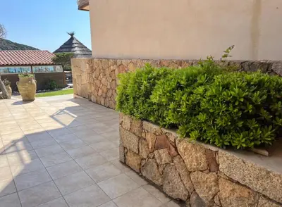 a stone retaining wall with a hedge next to a building at Hôtel Lilium Maris in Sartène