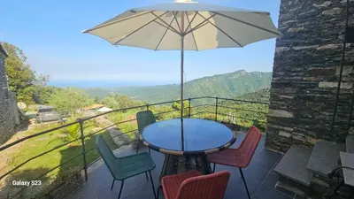 a table and chairs on a balcony with an umbrella at Domaine Colonna-Santini Gîte avec Piscine & Spa, Vue Mer et Montagnes in Porri