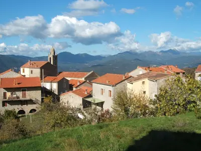 a group of buildings with a church and mountains at Casa Di Minnana in Petreto-Bicchisano