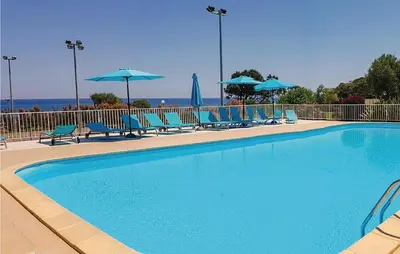 a swimming pool with blue chairs and umbrellas at 3 Bedroom Lovely Home In Cervione in Cervione