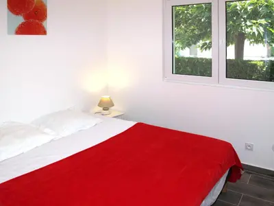 a bedroom with a red blanket on a bed with two windows at Holiday Home A Suara-1 by Interhome in Ghisonaccia