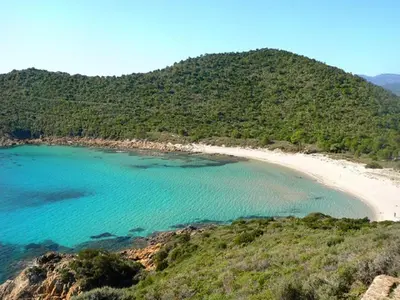 a beach with blue water and a hill at Marina Di Fautea in Olmucciu