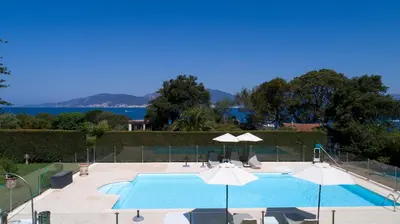 a swimming pool with umbrellas and the water at Villas les Residences de Scaglione in Porticcio