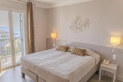 a white bedroom with a bed and a balcony at Hotel Maquis et Mer in Sari Solenzara