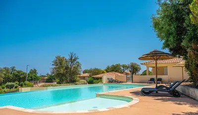 a swimming pool with two chairs and an umbrella at Résidence Odalys San Martinu in Sainte-Lucie de Porto-Vecchio