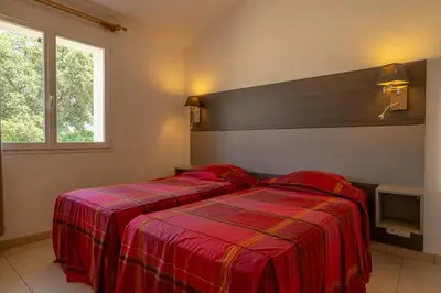 a bedroom with two beds with red sheets and a window at Résidence Odalys San Martinu in Sainte-Lucie de Porto-Vecchio