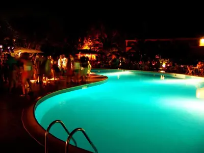 a group of people standing around a swimming pool at night at Vacancéole - Résidence Sognu di Mare in Linguizzetta