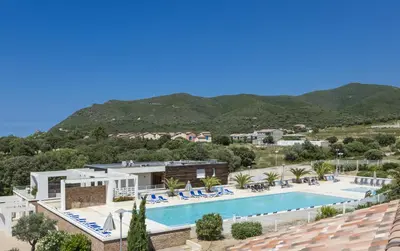 a resort with a swimming pool and mountains in the background at Résidence Odalys Les Villas de Bel Godère in Belgodère