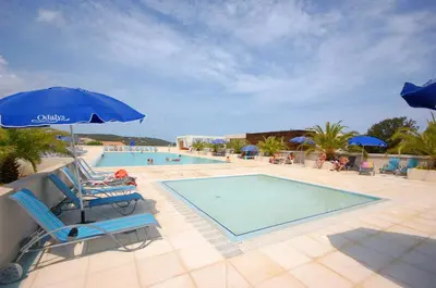 a swimming pool with two chairs and an umbrella at Résidence Odalys Les Villas de Bel Godère in Belgodère