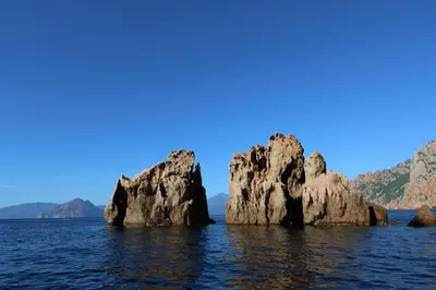 a group of rocks in the water with mountains in the background at Funtana a l'Ora in Porto Ota