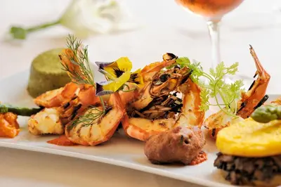 a plate of food with shrimp and a glass of wine at Hotel Stella Marina in Serriera