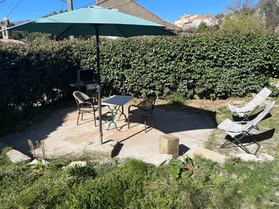 a table and chairs with an umbrella and a grill at Bas De Maison in Olivese