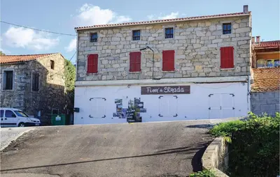 a white building with red shutters on a street at Amazing Apartment In Petreto-Biccisano in Petreto-Bicchisano