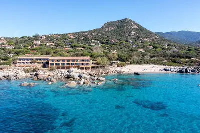 a building on a beach next to the water at Hôtel Abbartello in Olmeto