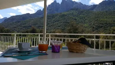 a table with drinks on a balcony with mountains in the background at Le Méditerranée in Porto Ota