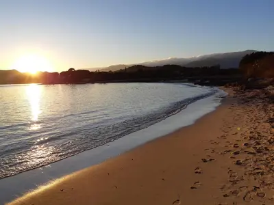 a beach with the sun setting over the water at Résidence Terre et Mer in Sainte-Lucie de Porto-Vecchio