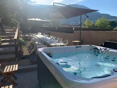 a hot tub on a patio with tables and an umbrella at Gîtes les Chalets Vezzani Spa in Vezzani