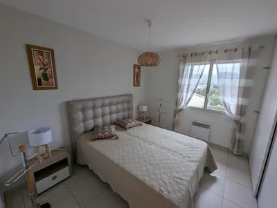 a white bedroom with a bed and a window at Les Terrasses De Vignola in Porto-Vecchio