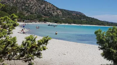 a group of people on a beach with a boat in the water at Locations Résidence Rocca Rossa Palombaggia classées 3 étoiles in Porto-Vecchio
