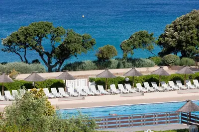 a swimming pool with chairs and the ocean in the background at Hotel Club Marina Viva in Porticcio