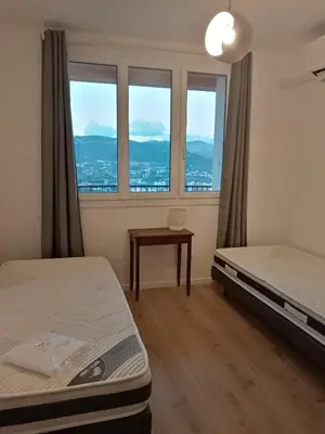 a room with two beds and a table and windows at Appartement Lumineux Vue Panoramique in Ajaccio