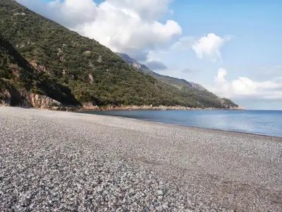 a rocky beach next to the ocean with a mountain at Hôtel & Résidence Le Subrini in Porto Ota