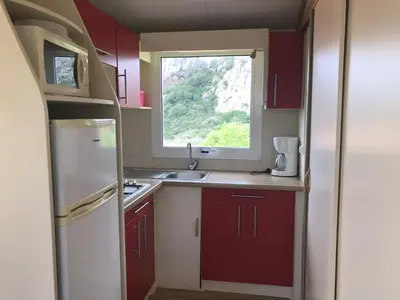 a small kitchen with red cabinets and a window at Camping Trinité in Bonifacio