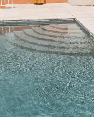 a swimming pool with blue water and steps at Hôtel Idéal in Porto Ota