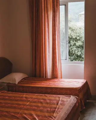 two beds in a room with a window at Hôtel Idéal in Porto Ota