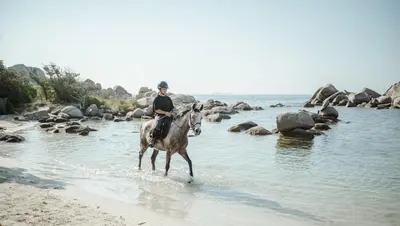 a man riding a horse through the water on the beach at Ranch Campo Palombaggia in Porto-Vecchio