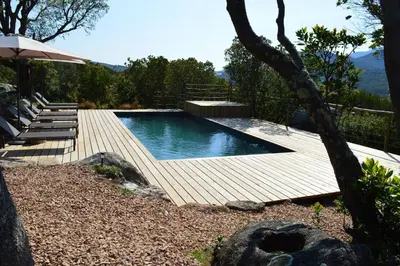 a swimming pool with a wooden deck and an umbrella at Les Petites Maisons in Sotta