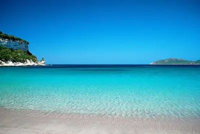 a beach with clear blue water and mountains in the background at Bonifacio 5 minutes du port et plage - clim & piscine in Bonifacio