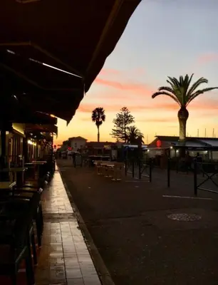 a street with tables and chairs and palm trees at sunset at Magnifique appartement devant la plage in Propriano