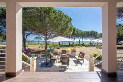 a porch with chairs and a table and an umbrella at MAISONS BORD DE MER- MARINE DE SORBO - Gîtes 3 épis in Pinarellu