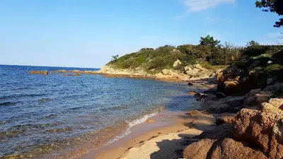 a beach with rocks and the ocean on a sunny day at Mini Villa à 100m de la mer avec prise de recharge élec privative in Sari Solenzara