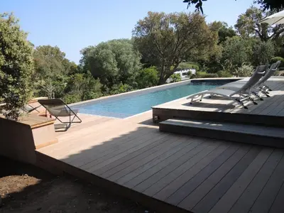 a swimming pool with two chairs and a wooden deck at Les Hauts de la Testa in Sainte-Lucie de Porto-Vecchio