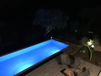 a blue swimming pool at night with chairs around it at Les Hauts de la Testa in Sainte-Lucie de Porto-Vecchio