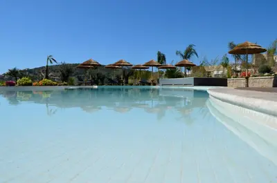 a swimming pool with blue water and umbrellas at Résidence de Tourisme Mare e Macchia in Tizzano