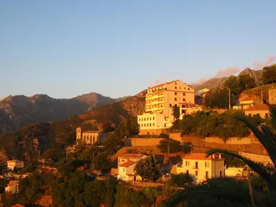 a town on a hill with mountains in the background at Hôtel Restaurant Sole e Monte in Cuttoli-Corticchiato