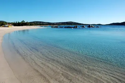 a beach with blue water and rocks in the distance at Cala di Sole Lecci in Porto-Vecchio