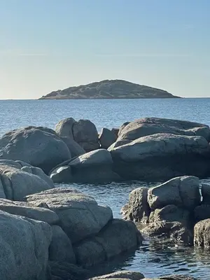 a group of rocks in the water with an island in the background at Cala di Sole Lecci in Porto-Vecchio