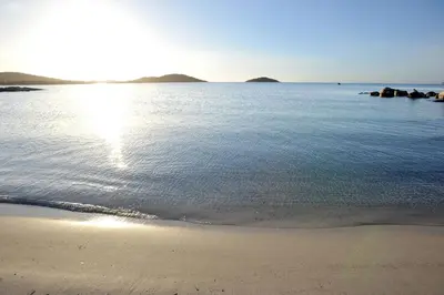 a beach with the sun reflecting on the water at Cala di Sole Lecci in Porto-Vecchio