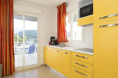 a kitchen with yellow cabinets and a view of a balcony at Résidence Odalys Casa d'Orinaju in Oletta