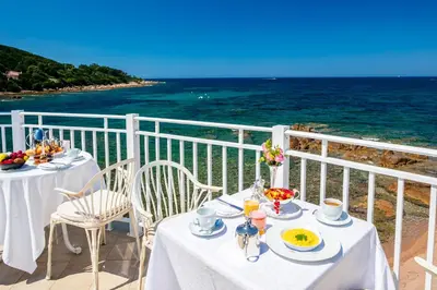 a table with plates of food on a balcony overlooking the ocean at Hotel Le Maquis in Porticcio